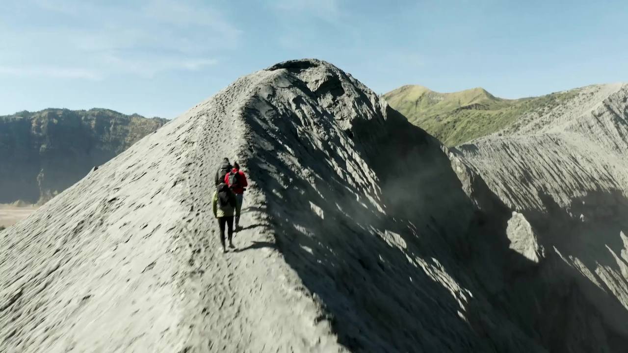 Montañeros caminan por una arista hacia la cima, vistos desde un dron